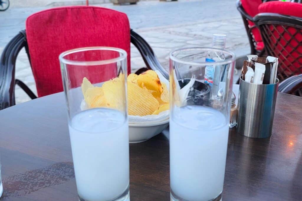 Two glasses of Greek ouzo served over ice with a side of potato chips