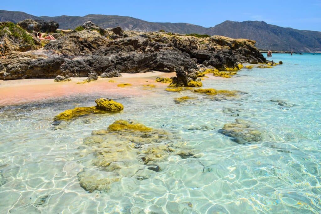 Translucent turquoise water along a rocky shoreline with pink sand